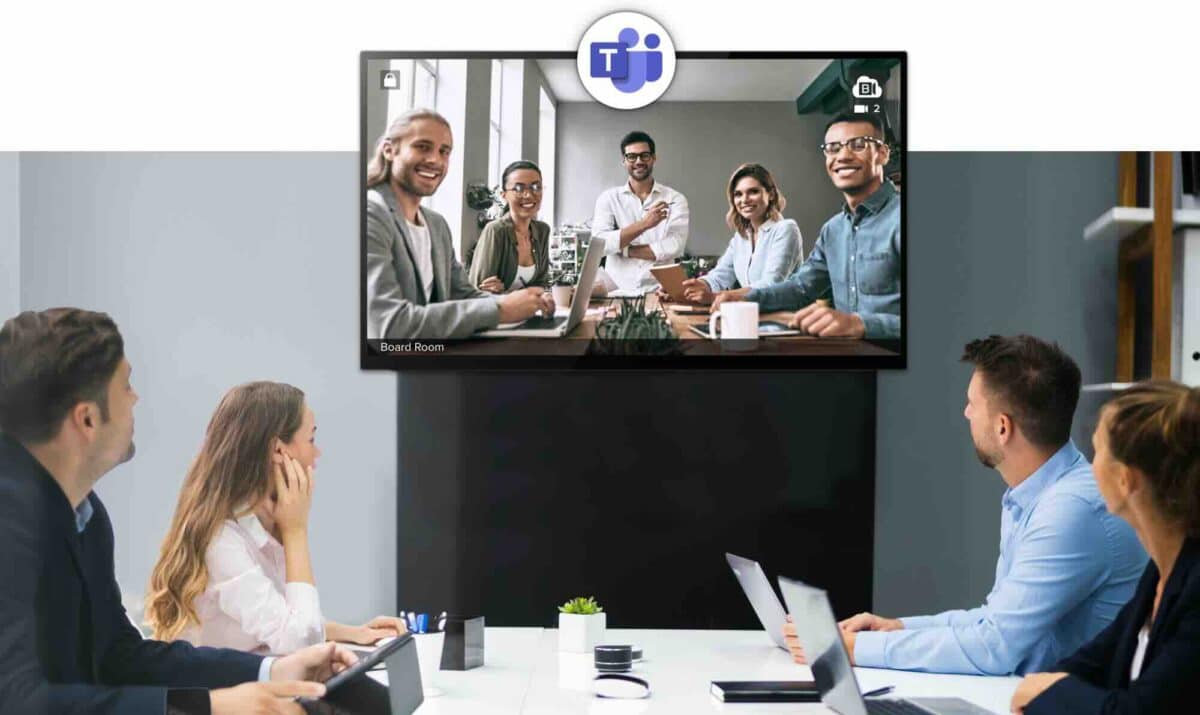 Ein Team sitzt in einem modernen Konferenzraum vor einem großen Bildschirm und nimmt an einer Microsoft Teams-Videokonferenz teil – ideal für hybride Meetings mit standardisierten Videokonferenzsystemen und Raumlösungen.