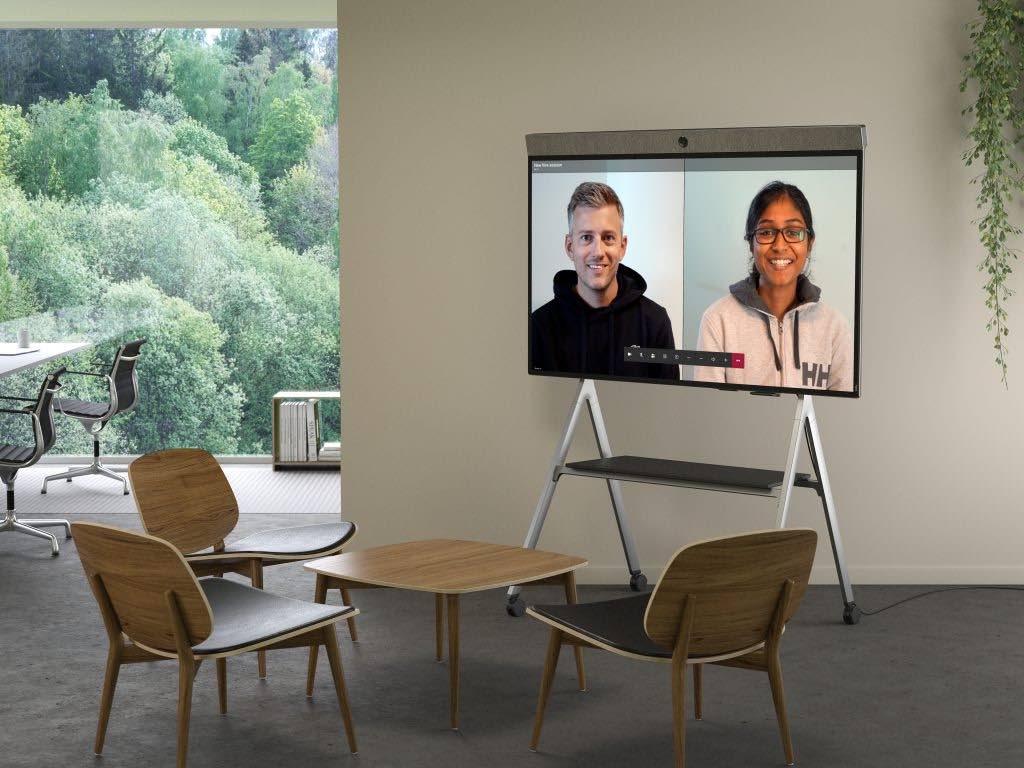 Neat Board mit mobiler Neat Bar auf Geräteständer – Videokonferenz in entspannter Lounge-Umgebung mit zwei Teilnehmenden