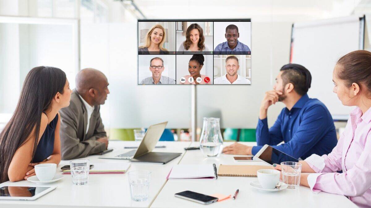 Gruppe bei hybrider Besprechung – Videokonferenz mit mehreren Teilnehmenden auf großem Bildschirm