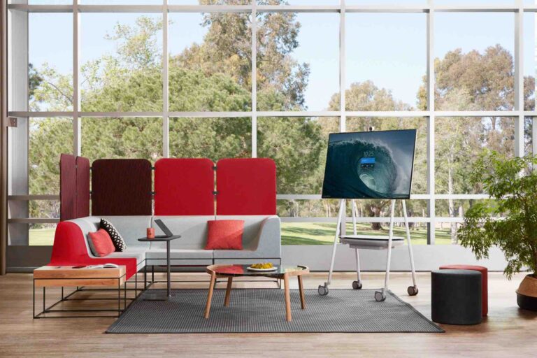 Microsoft Surface Hub 2S auf Rollgestell in einem offen gestalteten, barrierefreien Besprechungsraum mit Sitzmöbeln und großer Fensterfront