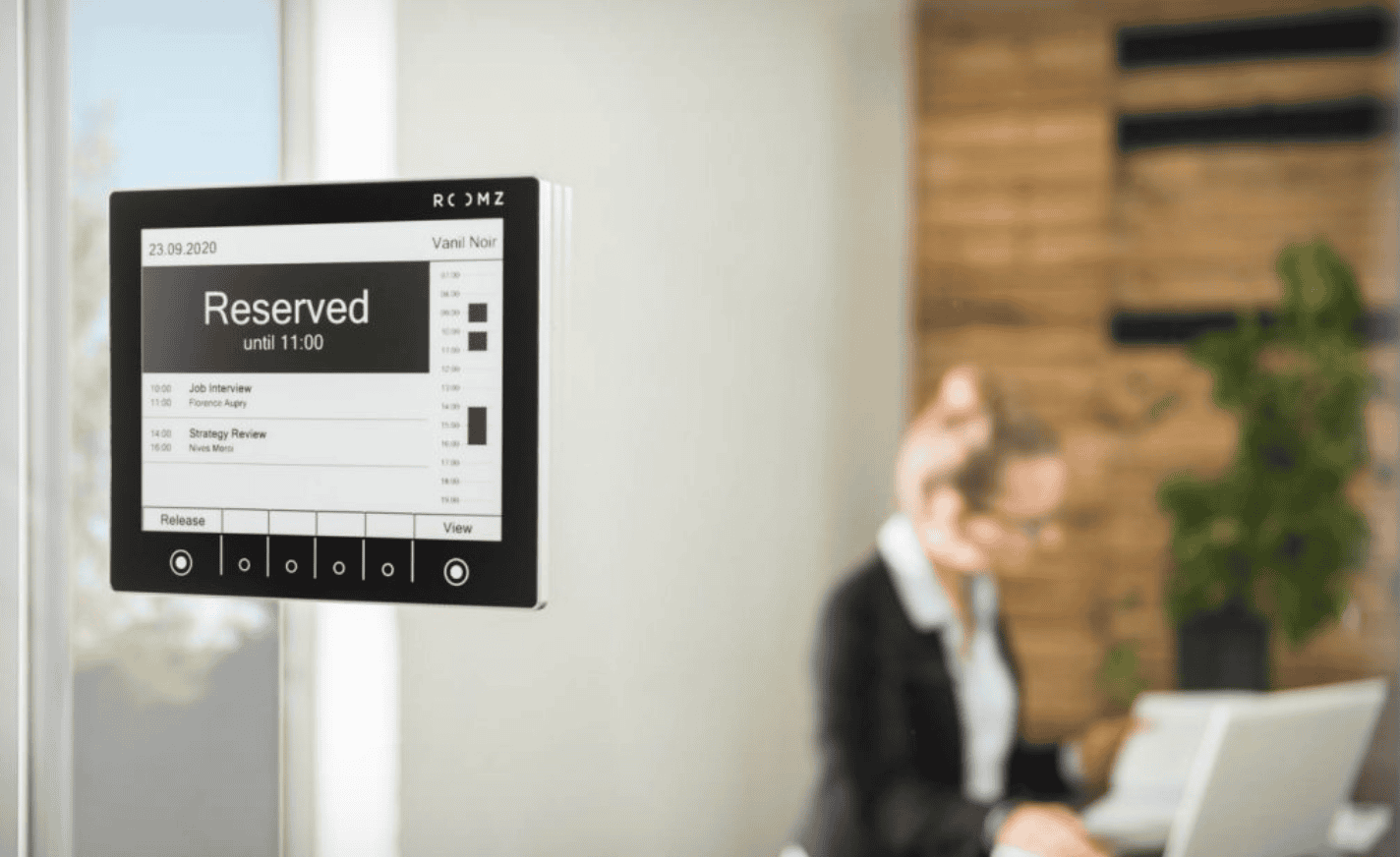 ROOMZ Display – Reservierungsanzeige für Besprechungsräume Ein ROOMZ-Display an einer Glaswand zeigt den Status „Reserved“ mit Uhrzeit und Rauminformationen an, um die Belegung von Besprechungsräumen transparent darzustellen.