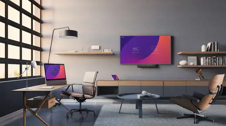 Ein stilvoll eingerichtetes Homeoffice mit Lounge-Charakter zeigt ein Cisco Board Pro an der Wand sowie einen Schreibtisch mit zusätzlichem Monitor – ideal für professionelle Videokonferenzen und hybride Arbeit im Remote-Umfeld.