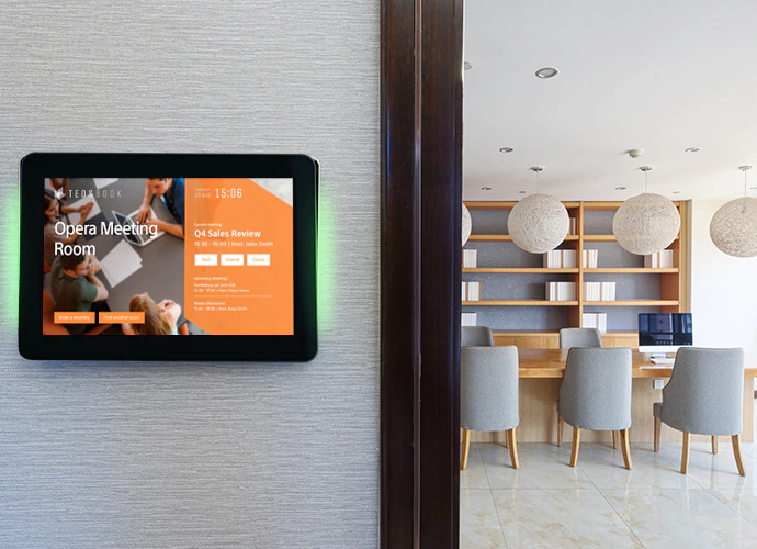 Ein Raumbuchungsterminal mit TEOS Software zeigt die aktuelle Belegung und Verfügbarkeit eines Meetingraums an – installiert an der Wand eines modernen Bürogebäudes, ideal für hybride Arbeitsplatzmodelle und effiziente Raumverwaltung.