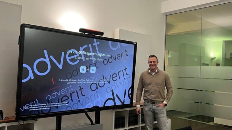 Ein Vertreter von adverit Compliance steht neben einem großformatigen CTOUCH Whiteboard in einem modernen Büro- oder Besprechungsraum, aufgenommen im Rahmen einer offiziellen Kundenreferenz zur täglichen Nutzung des interaktiven Systems.
