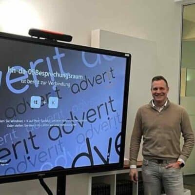 Marko Diepold, Managing Partner der adverit compliance GmbH & Co. KG, steht in einem modernen Besprechungsraum neben einem digitalen Whiteboard von Ctouch, das eine Konferenzoberfläche zeigt.