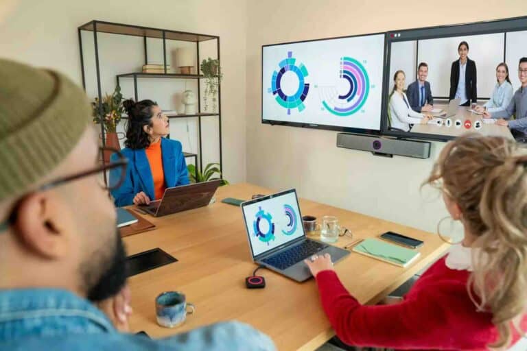 Zwei Personen nutzen in einem modernen Konferenzraum die Barco ClickShare Bar Pro zur drahtlosen Bildschirmfreigabe auf zwei großen Displays, ideal für hybride Meetings, Präsentationen und kollaboratives Arbeiten in Unternehmen.