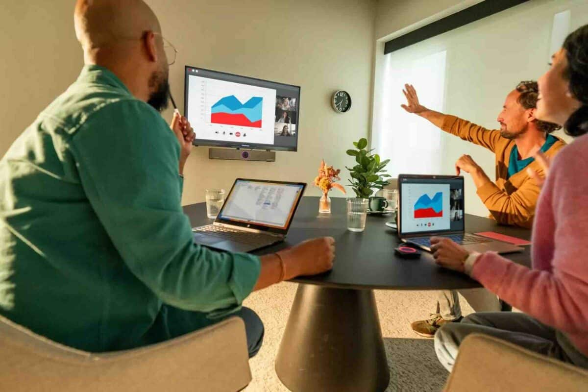 Drei Personen in einem kleinen Meetingraum präsentieren kabellos Inhalte über ein einzelnes Display mithilfe der Barco ClickShare Videobar Core – ideal für spontane Besprechungen und effiziente Zusammenarbeit in kompakten Räumen.