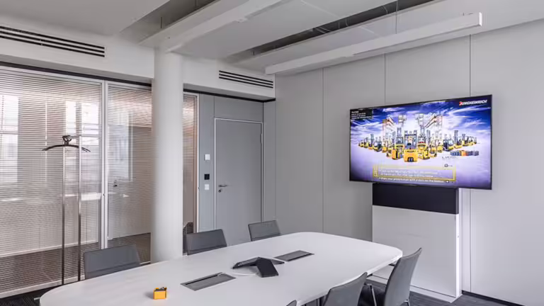 Die Fröscher Mico² 4 Medienstele mit großem Display ist in einem modern eingerichteten Konferenzraum installiert und verfügt über ein integriertes Technikmodul unterhalb des Bildschirms – ideal für hybride Meetings, Präsentationen und Business-Kommunikation.