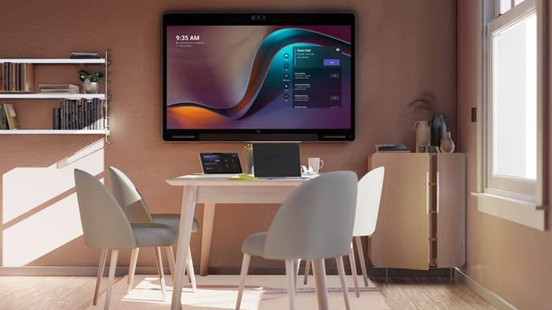 Ein kompakter Besprechungsraum für bis zu vier Personen ist mit Cisco Videokonferenztechnik für Microsoft Teams Rooms ausgestattet und zeigt die Startoberfläche auf einem Wanddisplay über dem Tisch.