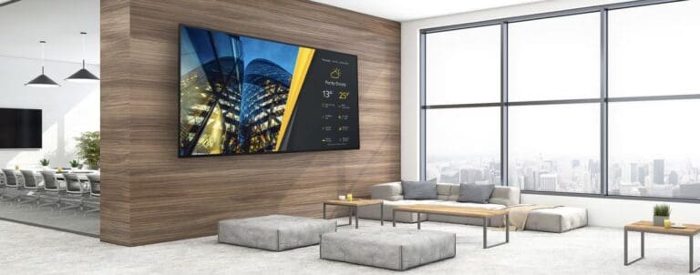 Ein eleganter Empfangsbereich mit bodentiefen Fenstern, modernen Lounge-Möbeln und wandmontiertem Sony BRAVIA Display zur Darstellung von Inhalten – ideal für Unternehmen, die Besucher stilvoll empfangen und informieren möchten.