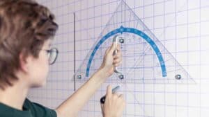 Ein Schüler arbeitet vor einem großen Touchdisplay mit kariertem Hintergrund; auf dem Bildschirm sind ein gezeichneter Bogen, Linien und ein geometrisches Werkzeug sichtbar.