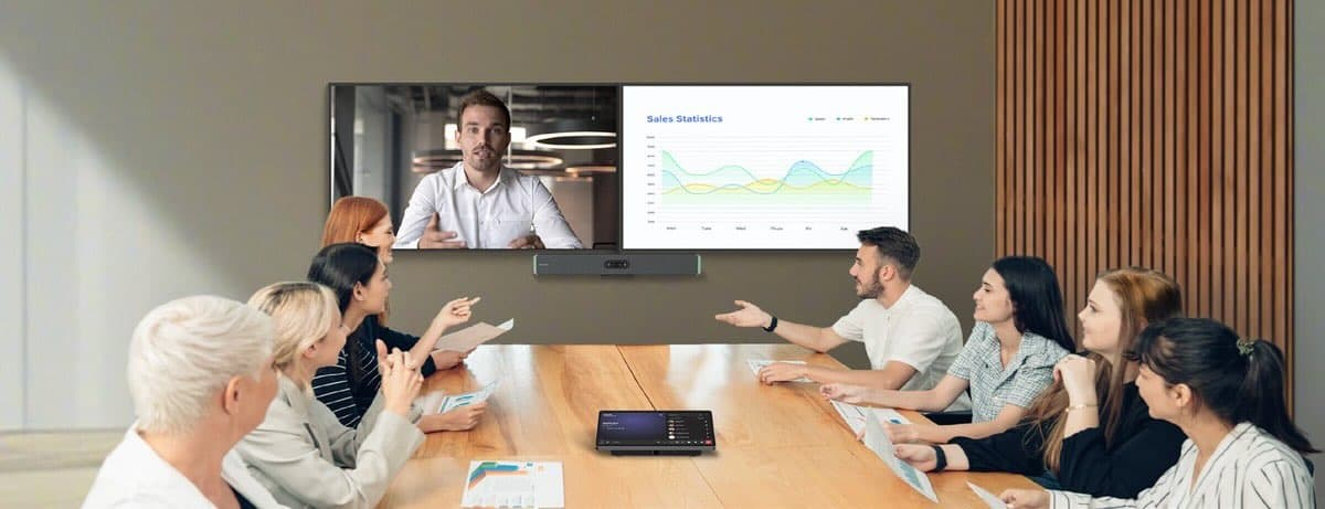MAXHUB XBar W70 Kit Videokonferenz im Konferenzraum Konferenzraum mit mehreren Personen an einem Holztisch, an der Wand ein großes Display mit Videokonferenz, darunter eine montierte Videobar.