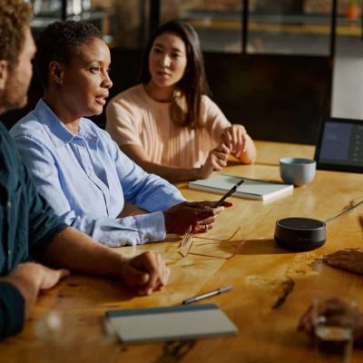 Ein Meetingraum mit hohen Decken, Backsteinwänden und großem Konferenztisch, an dem mehrere Personen sitzen; über ihnen sorgt ein Sennheiser TeamConnect Ceiling Mikrofon für exzellente Sprachaufnahme trotz herausfordernder Raumakustik – ideal für moderne Besprechungsräume mit Glas oder Beton.